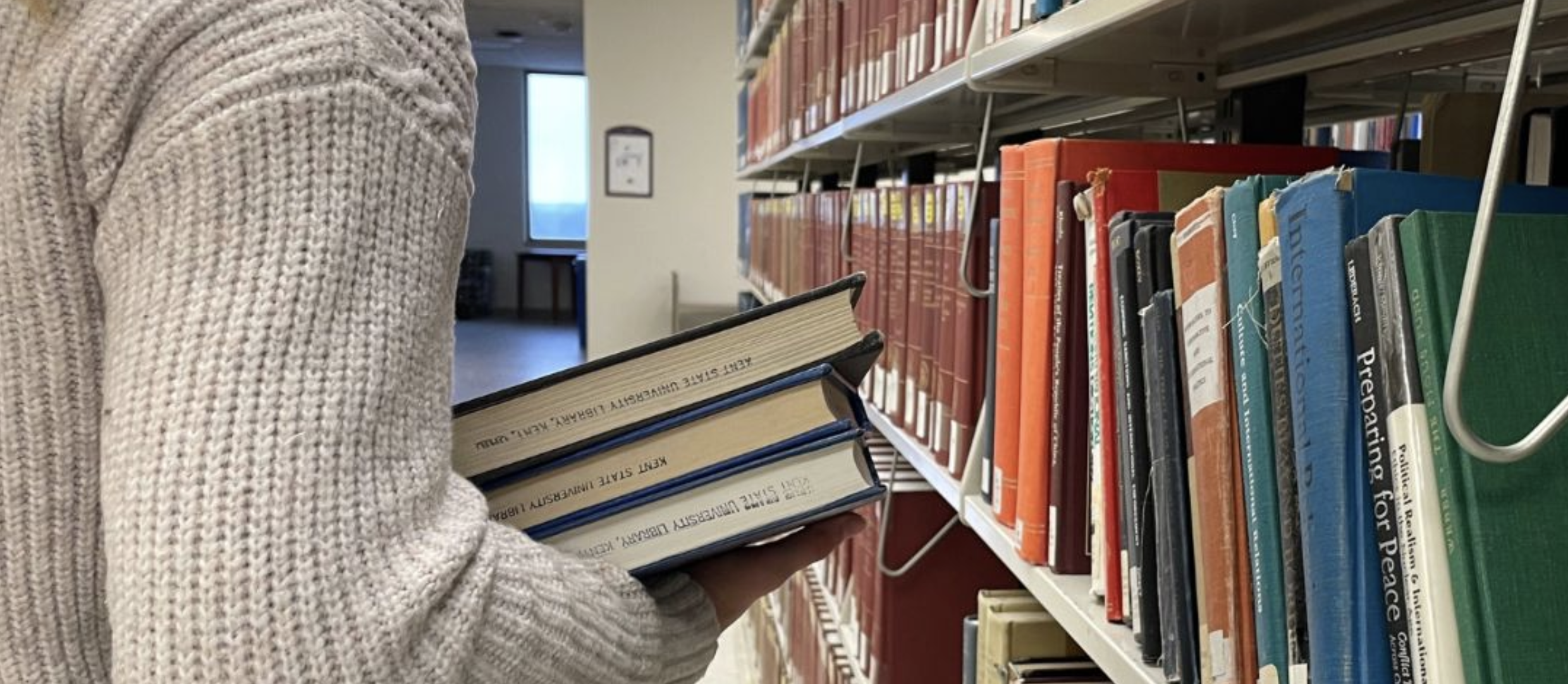 Student holding books while looking through a shelf