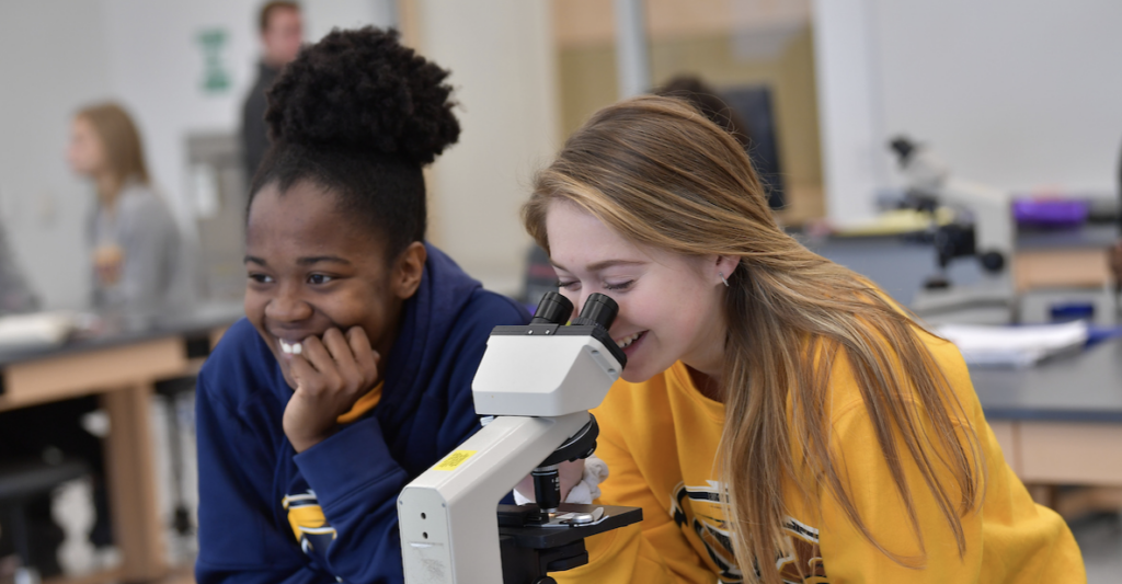 Two female students look at a microscope